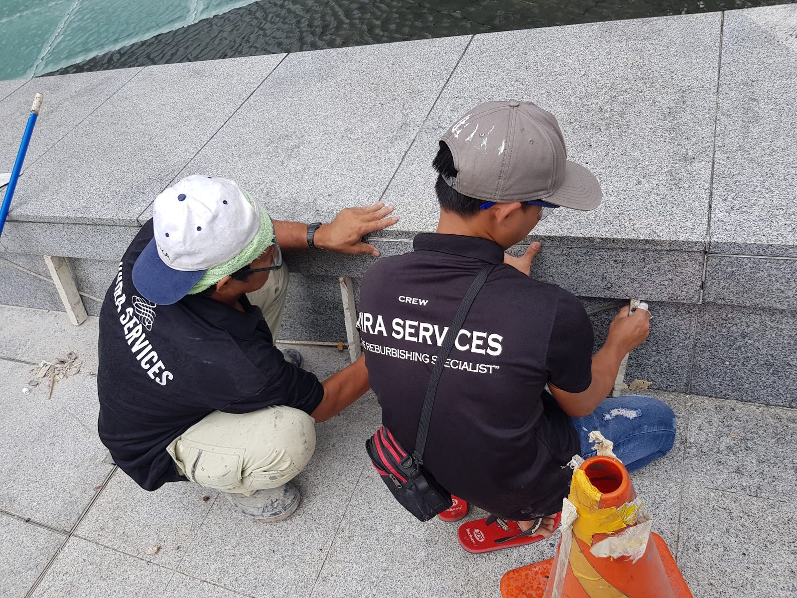 Two uniformed Wira Services crew members repointing granite on a poolside job